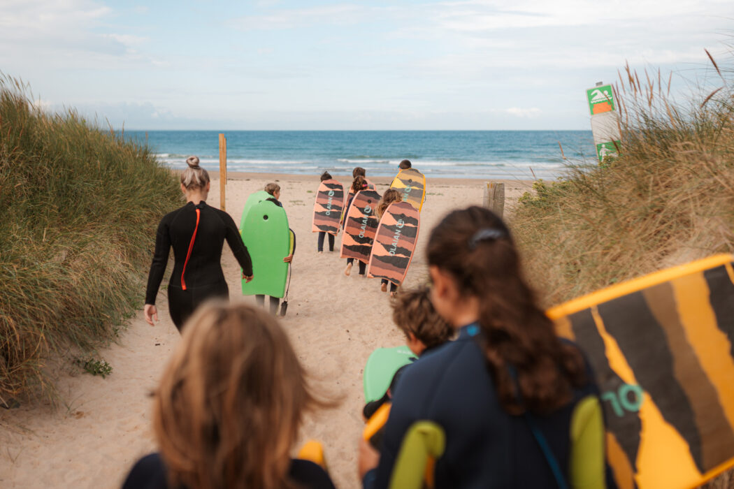 Enfants qui se dirigent vers la mer en combinaison de plongée et avec des bodyboard, à l'occasion De la Piscine à la Mer à la Plage du Rozel