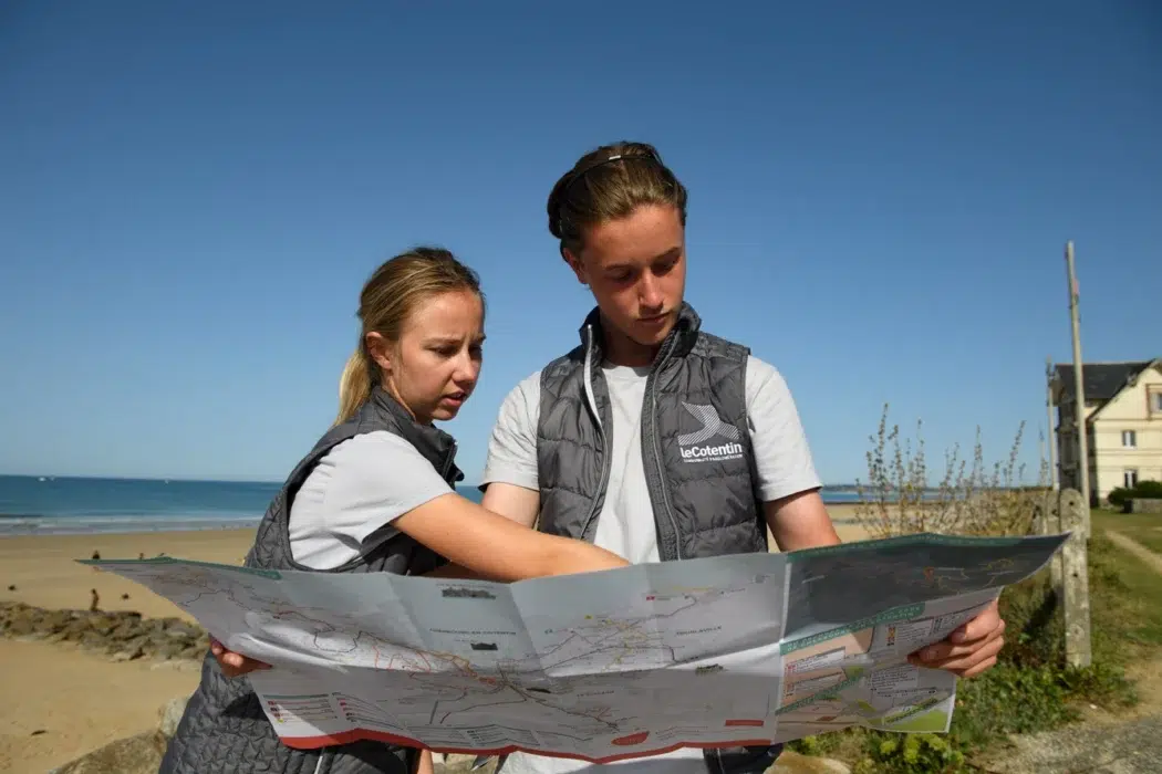 Deux Ambassadeurs du littoral consultent une carte du Cotentin sur la plage de Portbail.