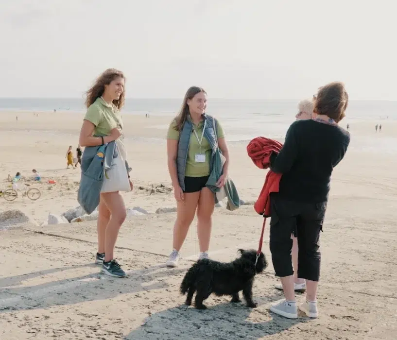 Des Ambassadeurs du littoral discutent avec deux promeneuses et son chien sur la plage.