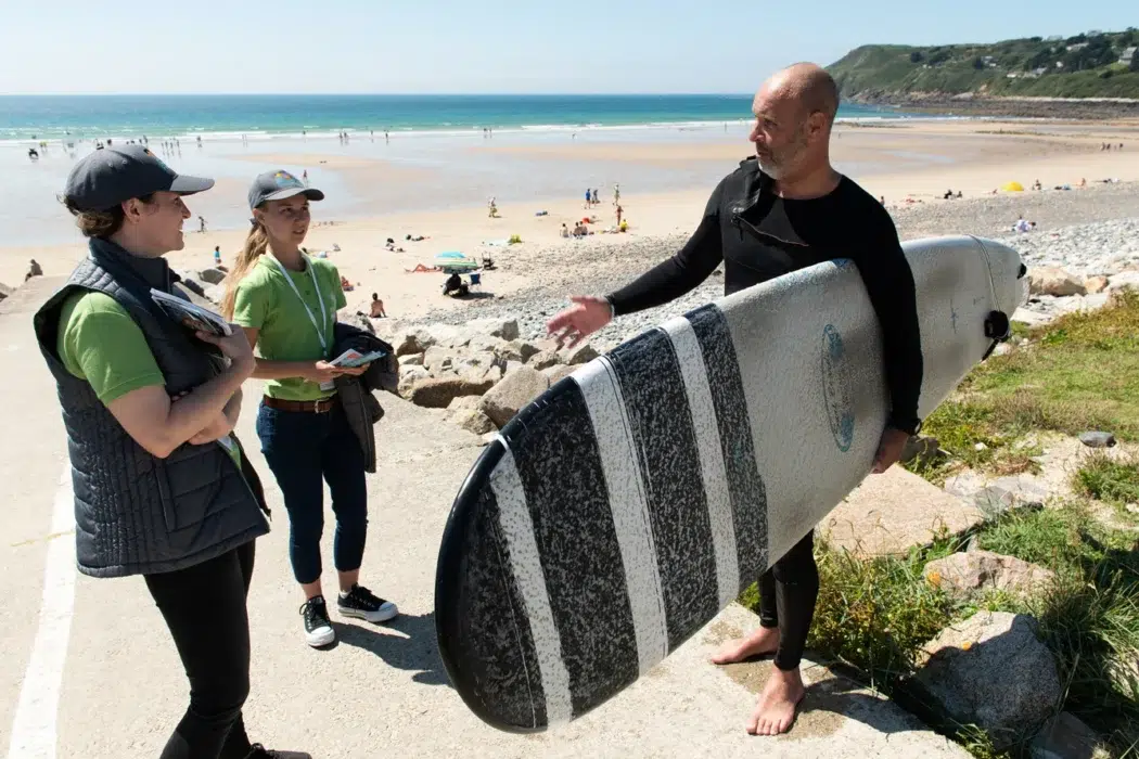 Des Ambassadeurs du littoral échangent avec un surfeur sur une plage du Cotentin.